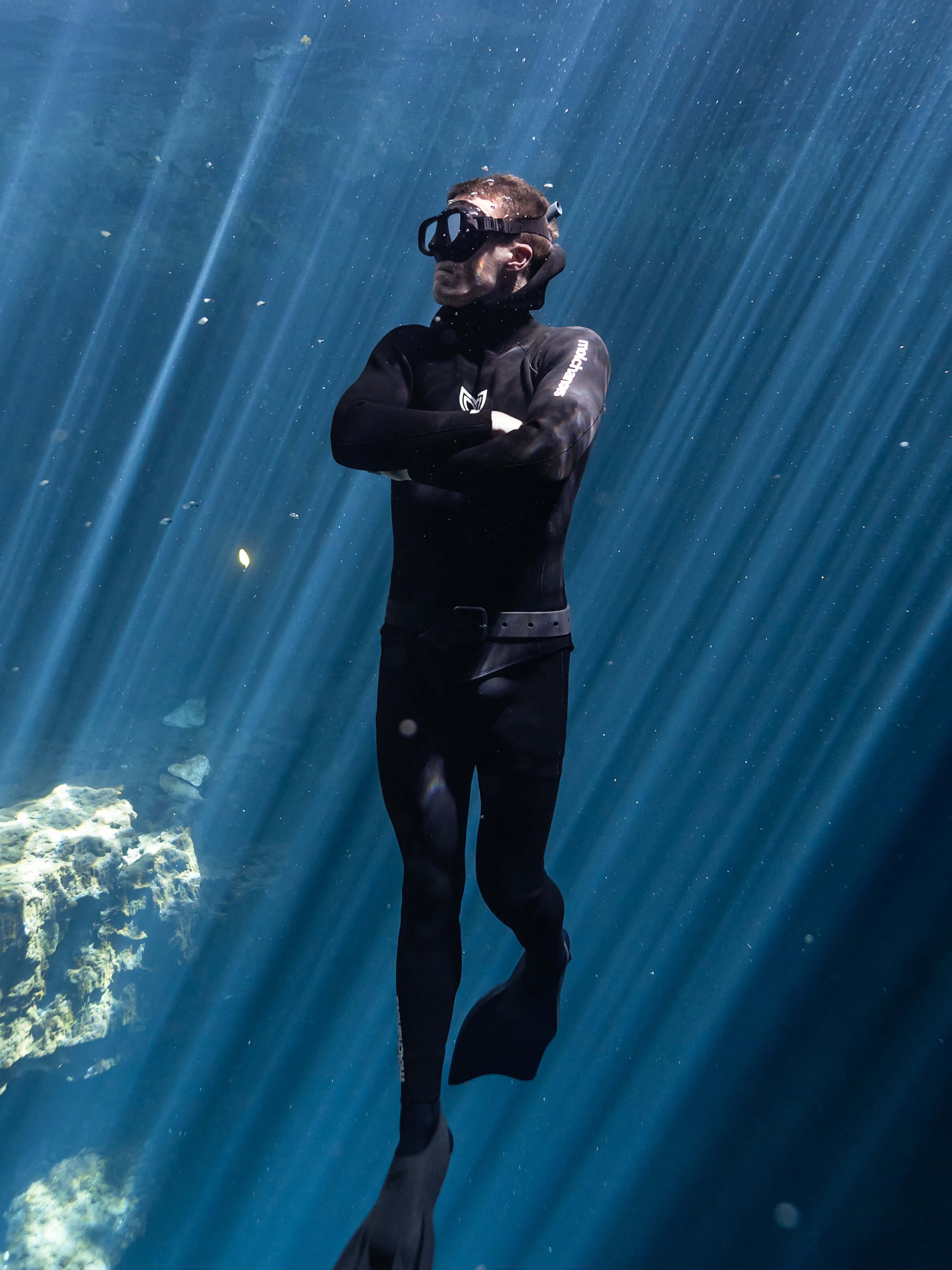 A diver wearing a black two piece 5mm wetsuit swimming amongst beams of light